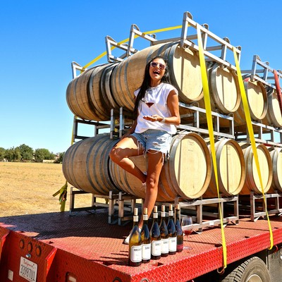 Popular wine influencer Elle Rodriguez (@themodernpour) with Turley Wine Cellars barrels and bottles of Sandlands Wines, parked at Lodi's Kirschenmann Vineyard.